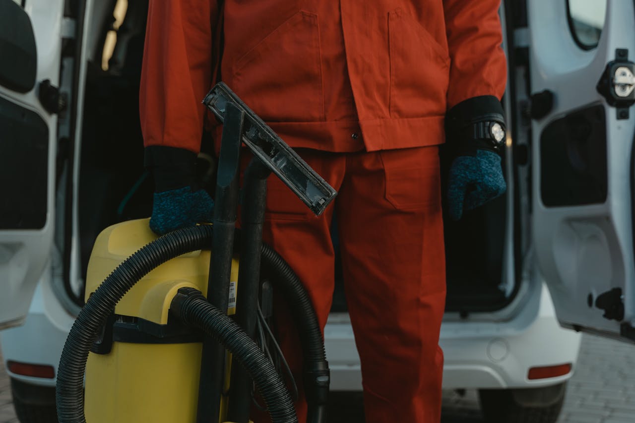 gallery-6 A professional cleaner in a red uniform holding a vacuum near a van, ready for service.