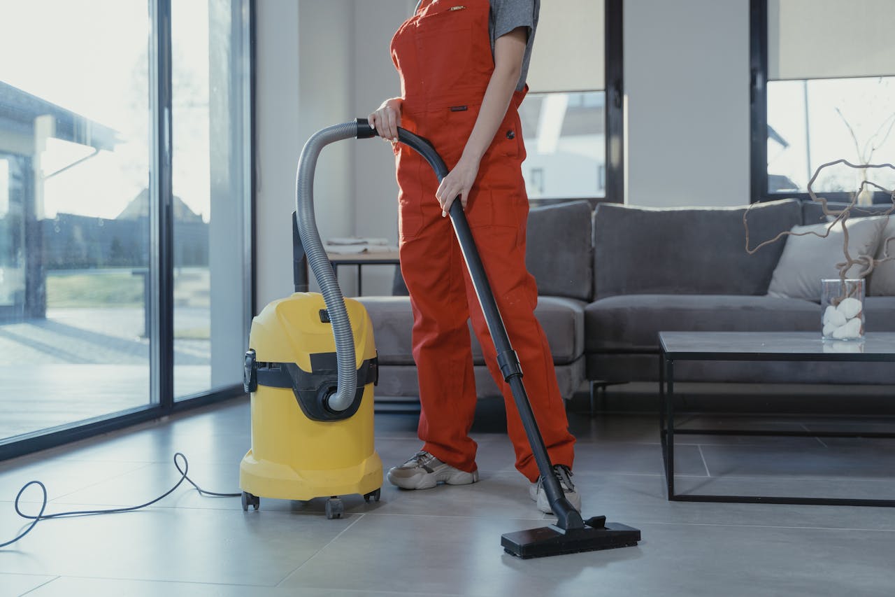 about-01 A professional cleaner in red coveralls vacuuming a modern living room with a yellow vacuum cleaner.